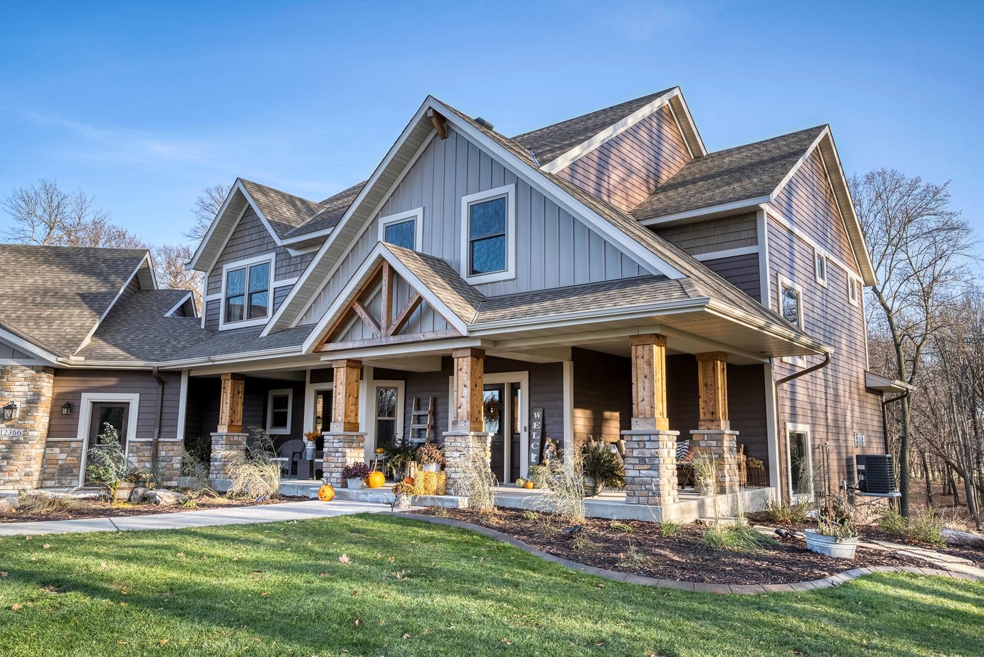Modern farmhouse with multiple gable rooflines, stone and siding exterior, wooden front porch columns, and manicured lawn