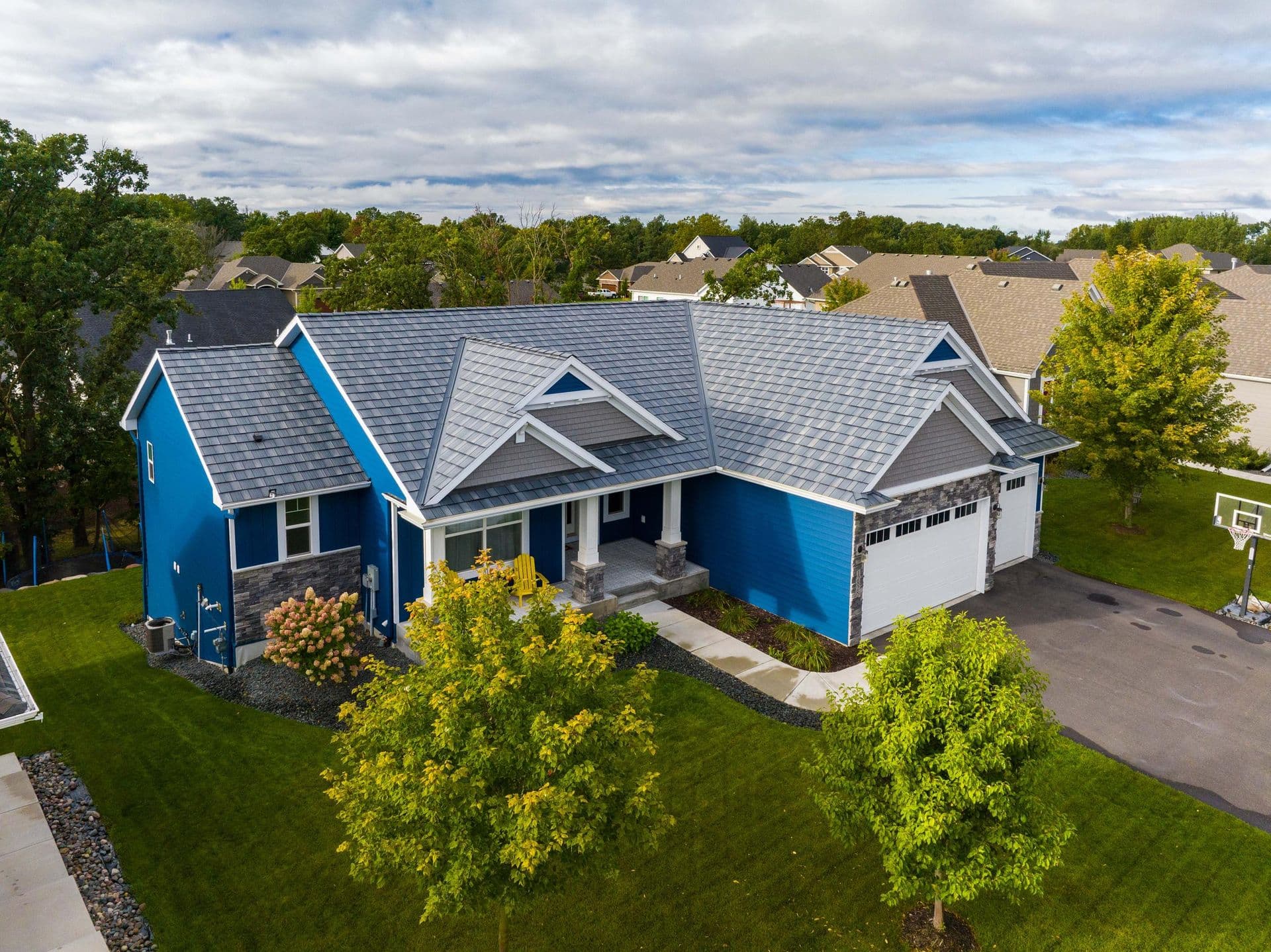 Modern two-story home with blue and white exterior, gray metal roof, front portico, attached garage, and landscaped yard in suburban neighborhood