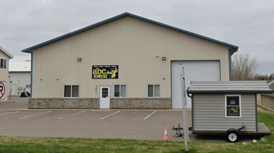 ABC Seamless metal building storefront with large garage door, white entrance, and display trailer in parking lot