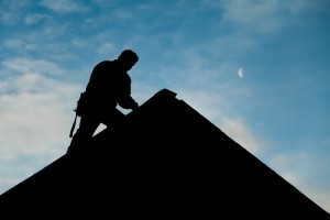 man working on roof of house with sky in background